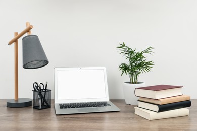 Photo of Stack of hardcover books, laptop and stylish lamp on wooden table indoors