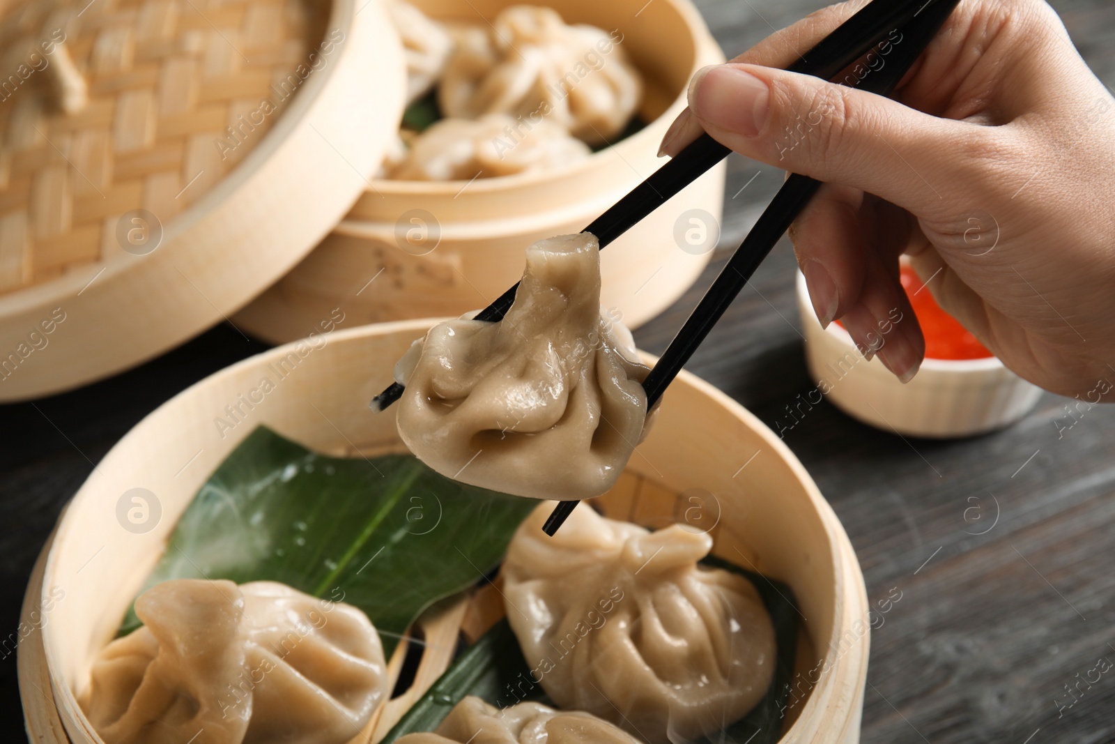 Photo of Woman cooking tasty baozi dumplings in bamboo steamer at table, closeup