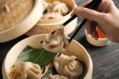 Photo of Woman cooking tasty baozi dumplings in bamboo steamer at table, closeup