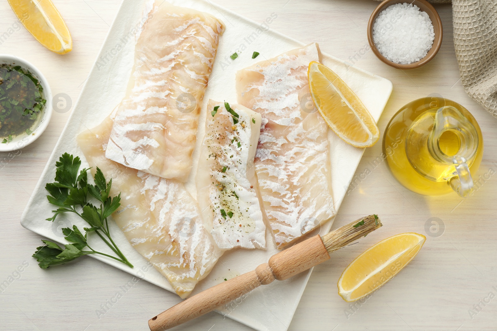 Photo of Fresh raw cod fillets with spices and lemon on white wooden table, flat lay