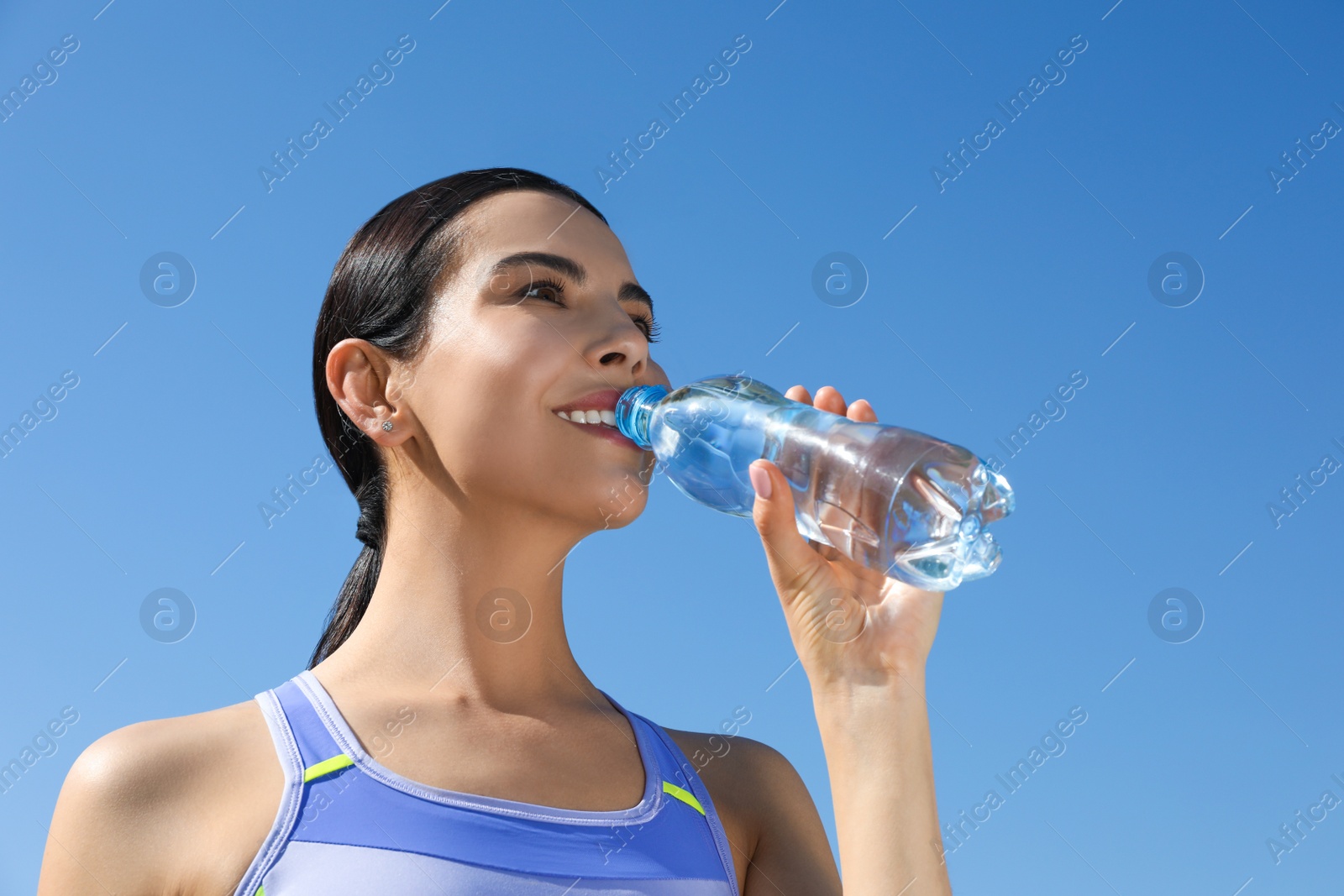 Photo of Beautiful young sportswoman drinking water outdoors. Refreshing drink