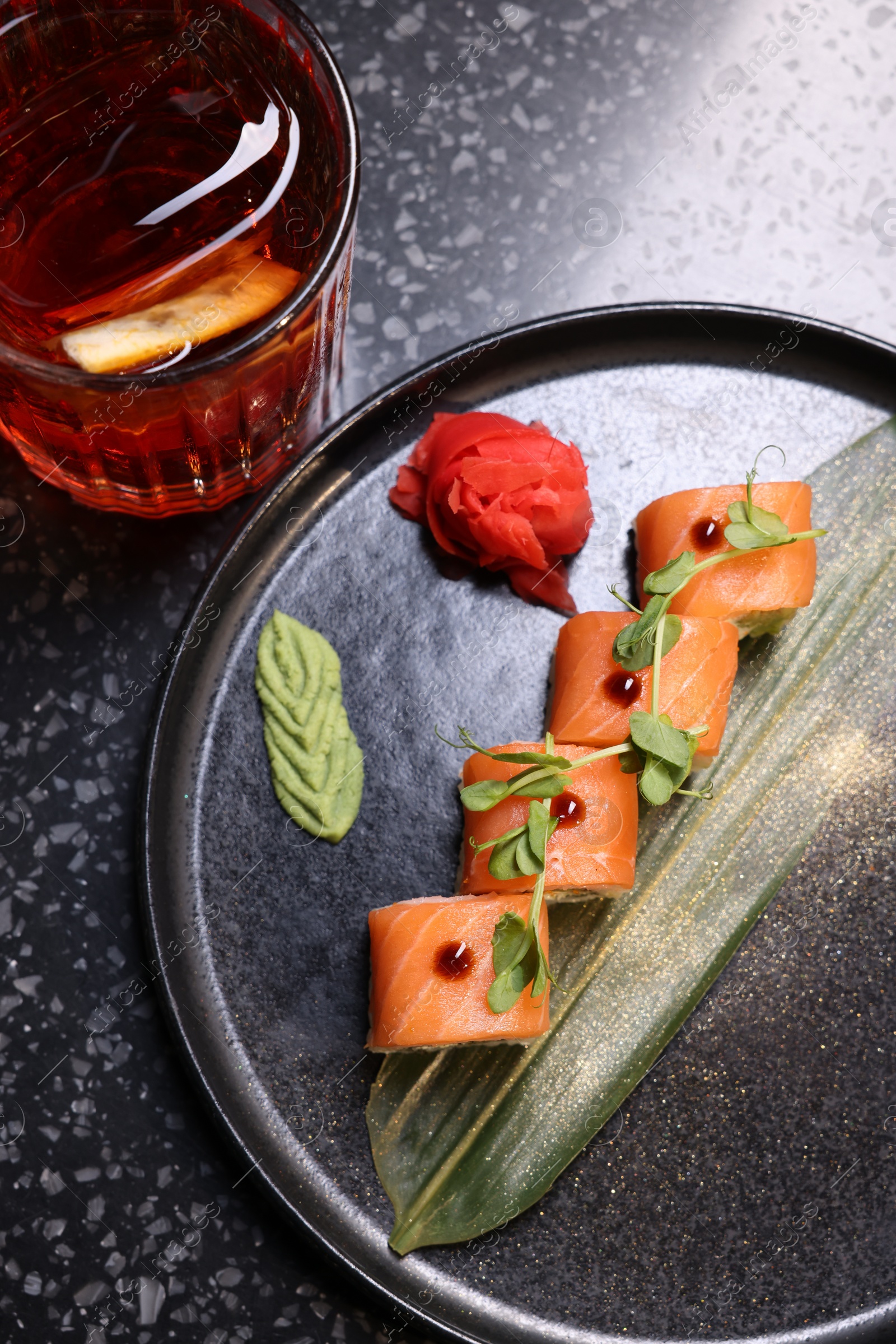 Photo of Delicious sushi rolls served with alcoholic Negroni cocktail on dark table, flat lay