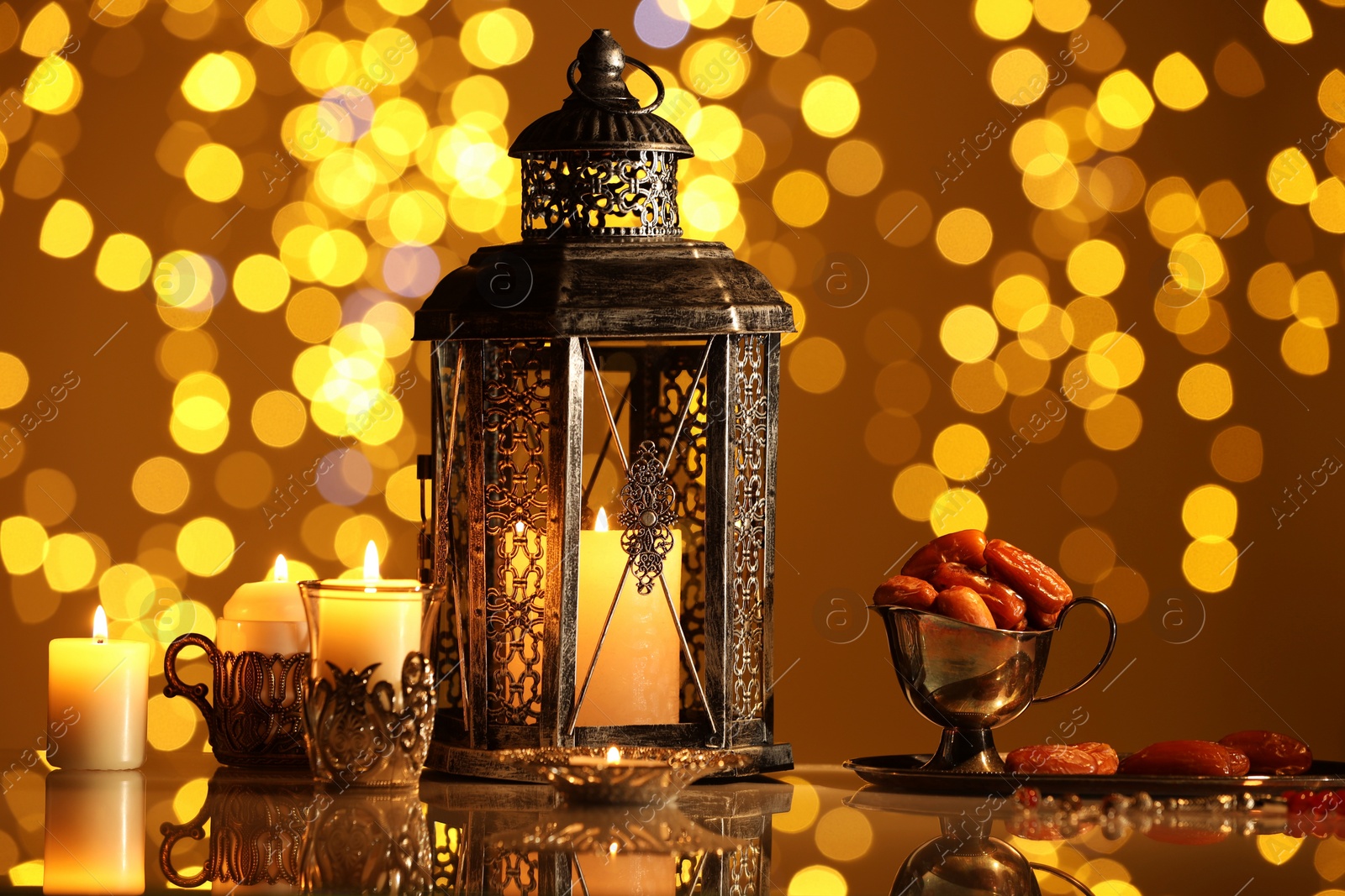 Photo of Arabic lantern, burning candles, dates and misbaha on mirror surface against blurred lights