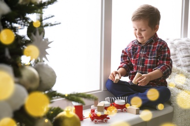 Photo of Cute little boy playing with toy train on window sill at home. Christmas atmosphere