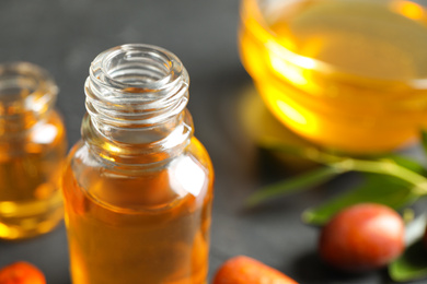 Jojoba oil in glass bottle on table, closeup view