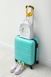 Photo of Suitcase packed for trip, shoes and accessories near white wall indoors