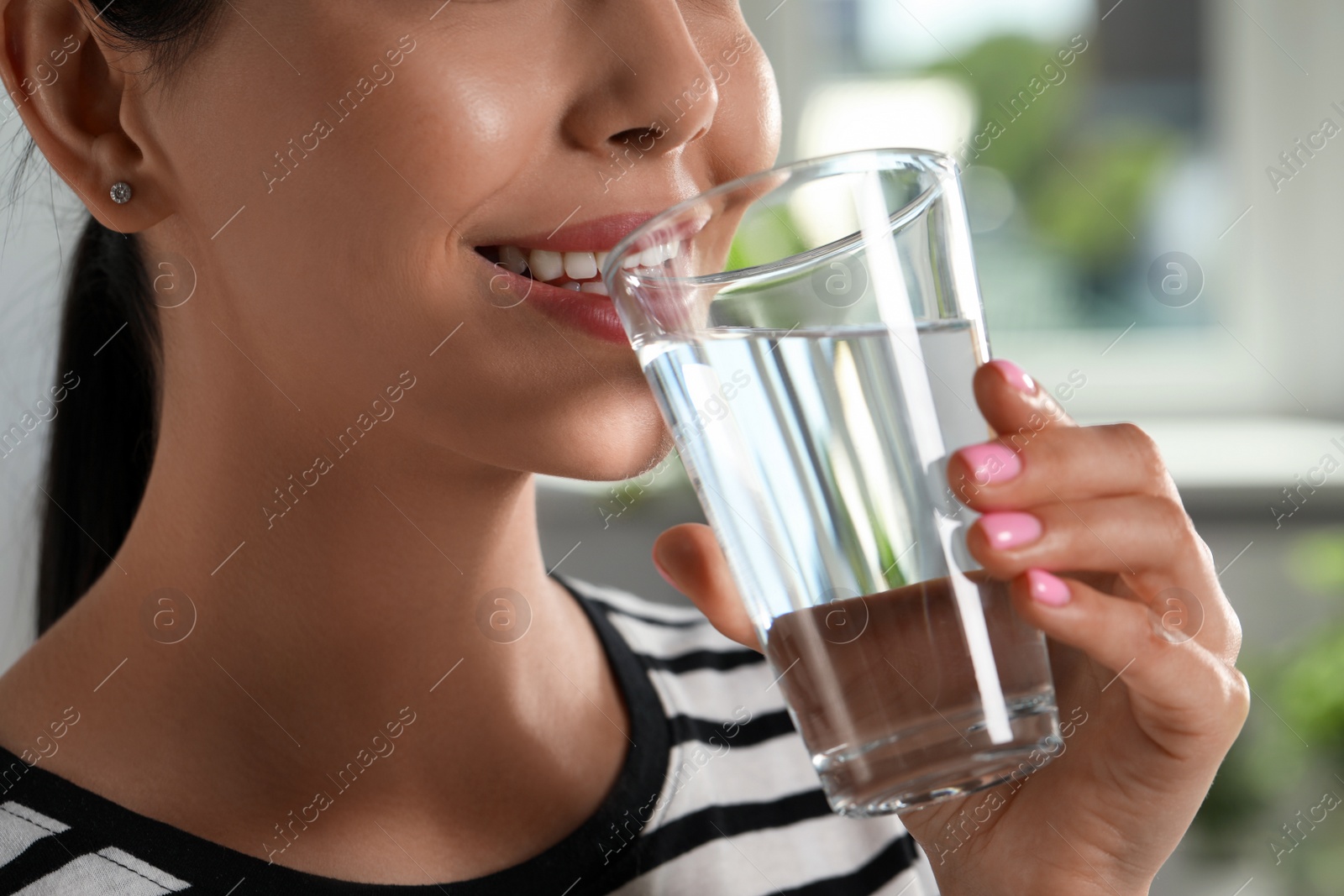 Photo of Young woman drinking water indoors, closeup. Refreshing drink