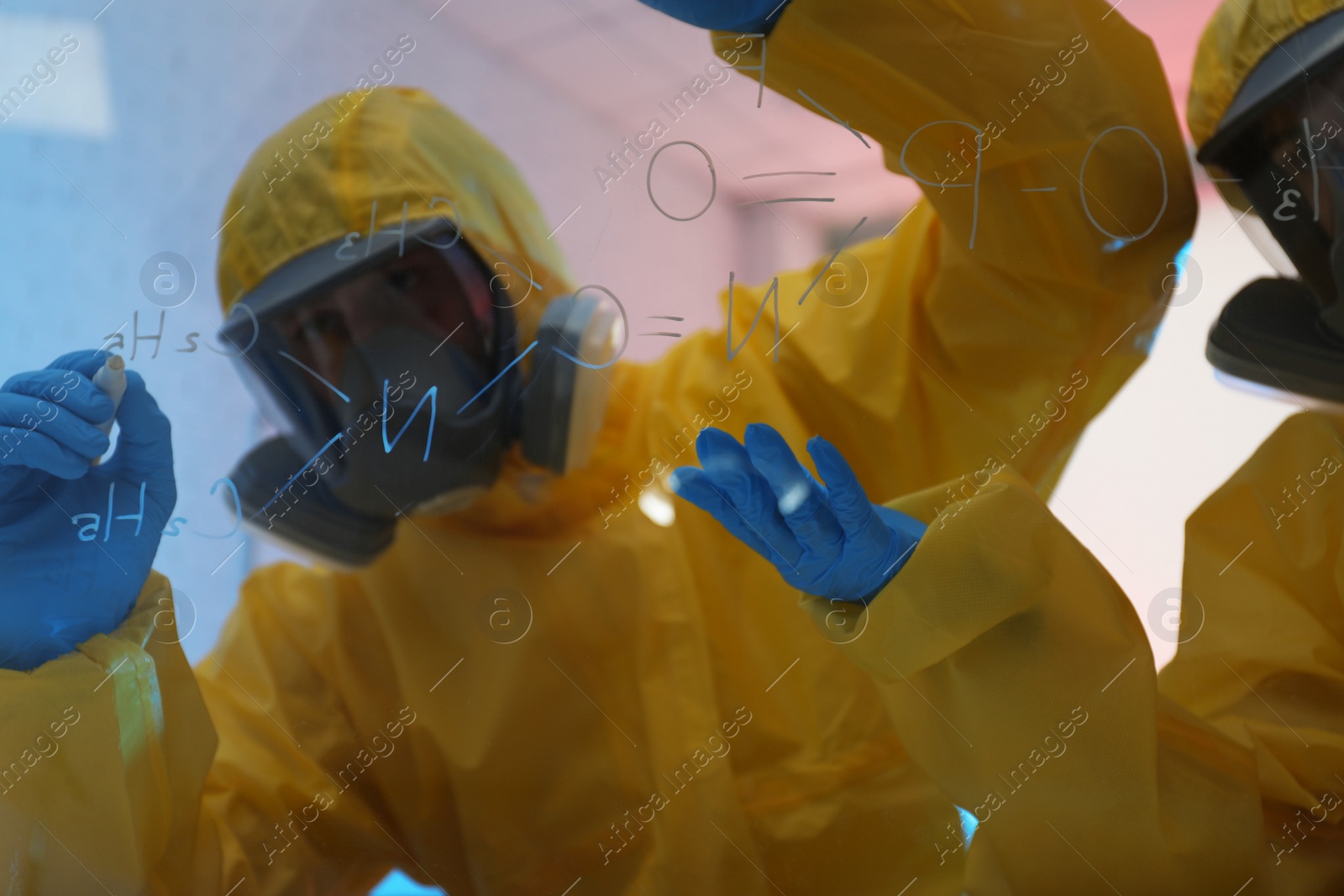 Photo of Scientists in chemical protective suits writing formula on glass board at laboratory. Virus research