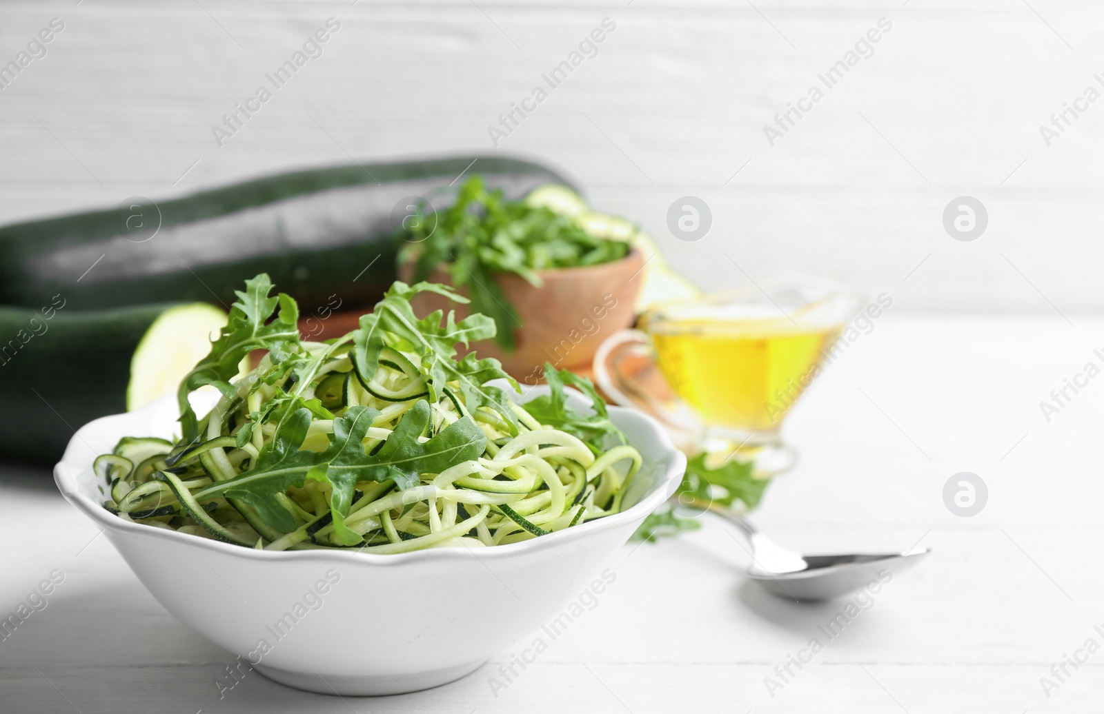 Photo of Delicious zucchini pasta with arugula in bowl on white wooden table