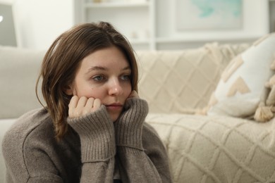 Sad young woman sitting near sofa at home, space for text