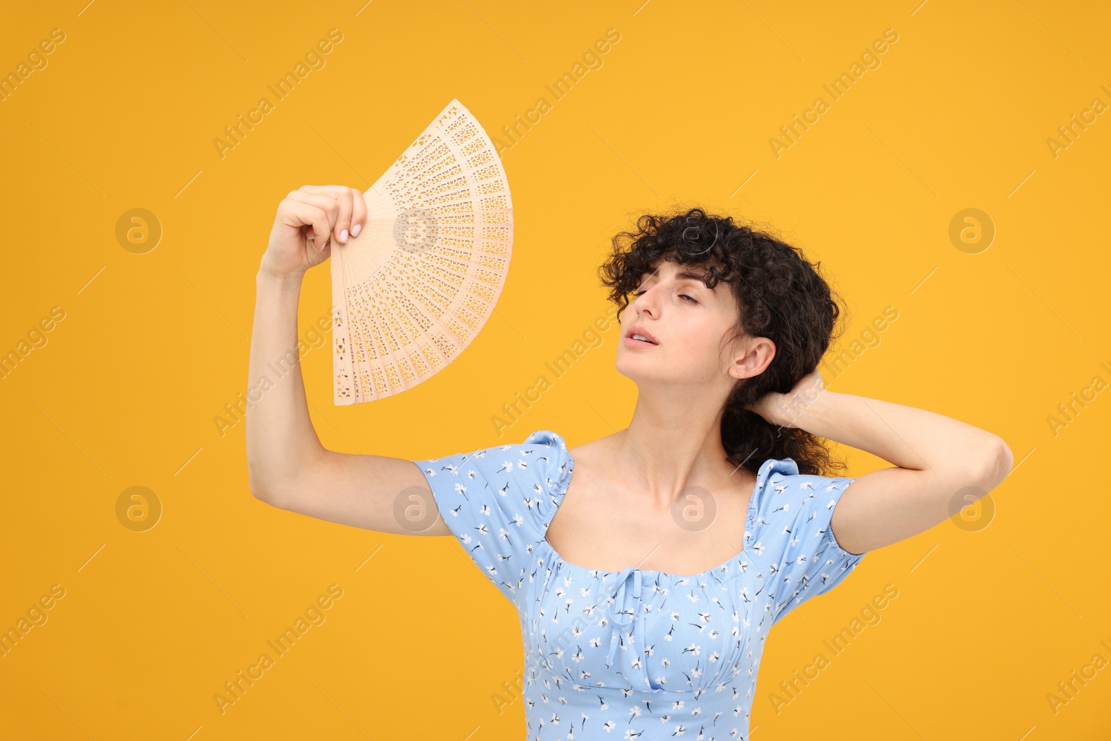 Photo of Woman with hand fan suffering from heat on orange background