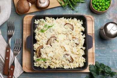 Delicious risotto with cheese and mushrooms on light blue wooden table, flat lay