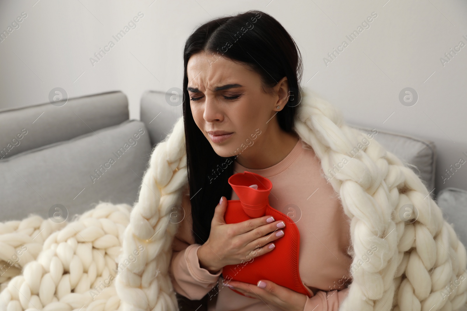 Photo of Ill woman with hot water bottle suffering from cold at home