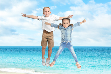 Image of Cute school boy and girl jumping on beach near sea. Summer holidays