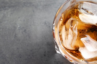 Glass of whiskey with ice cubes on grey background, top view. Space for text