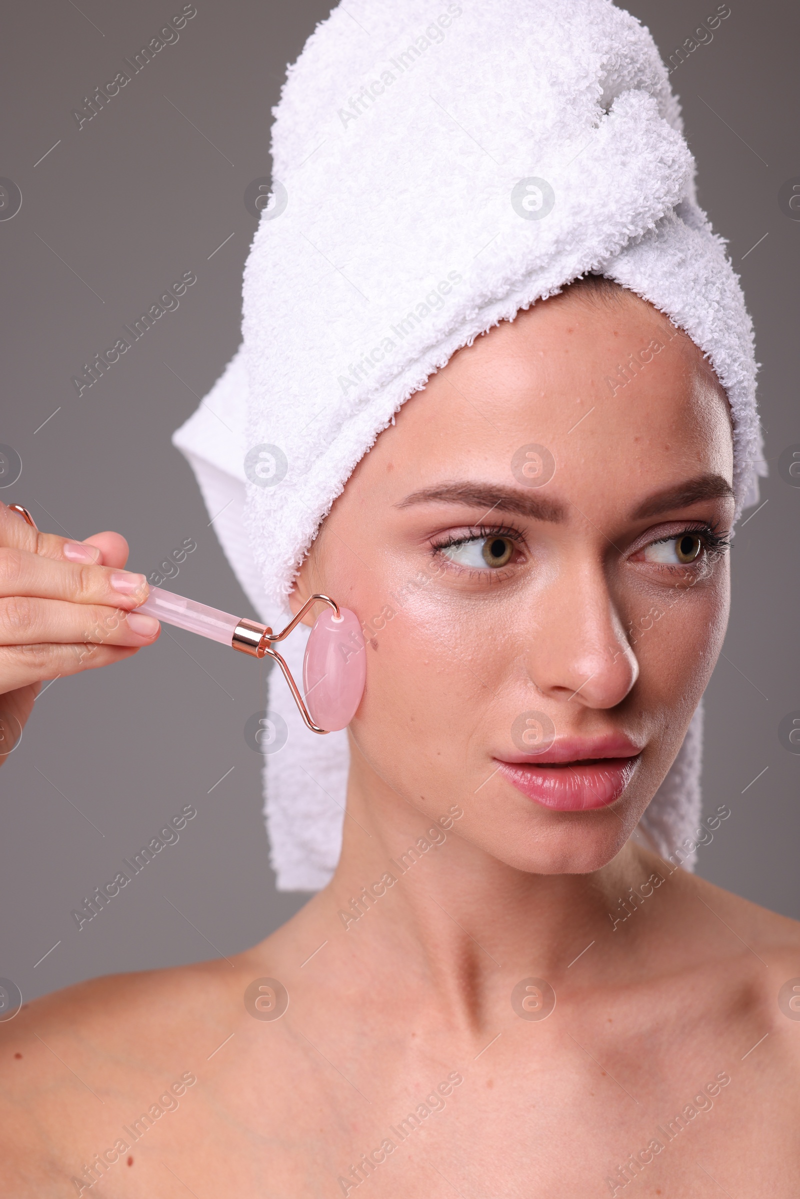 Photo of Young woman massaging her face with rose quartz roller on grey background