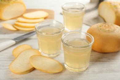 Photo of Glasses of fresh natural turnip juice, cut and whole roots on white wooden table