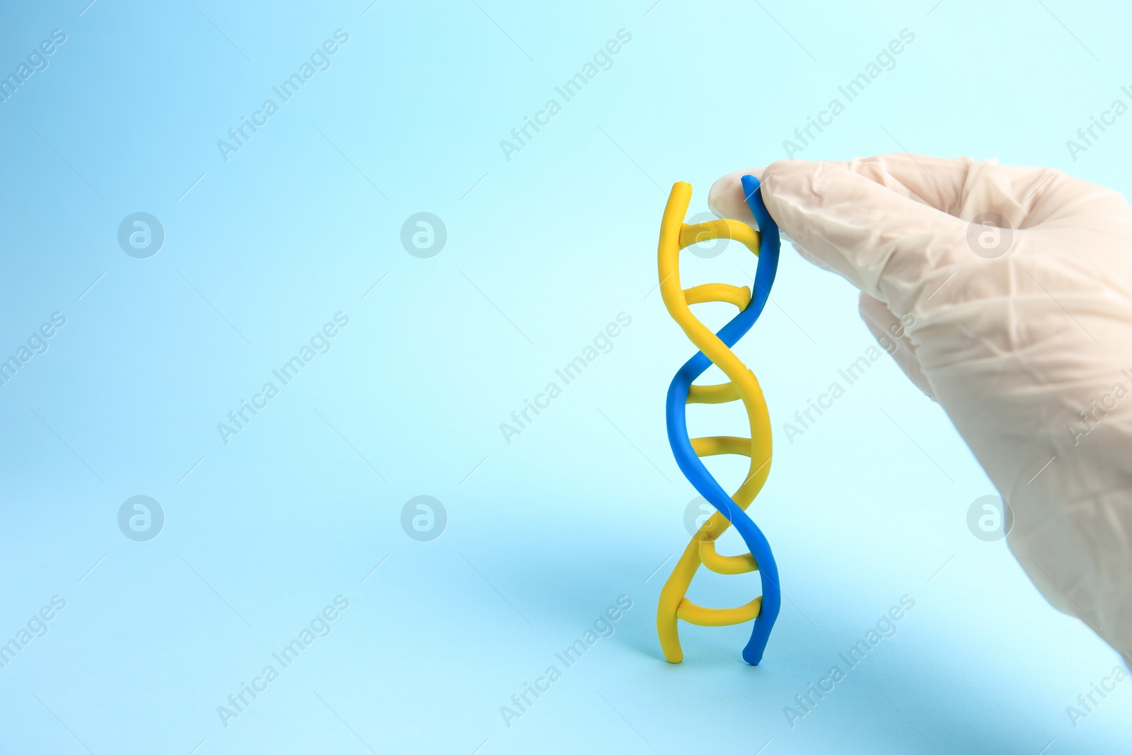 Photo of Scientist with DNA molecule model made of plasticine on light blue background, closeup. Space for text