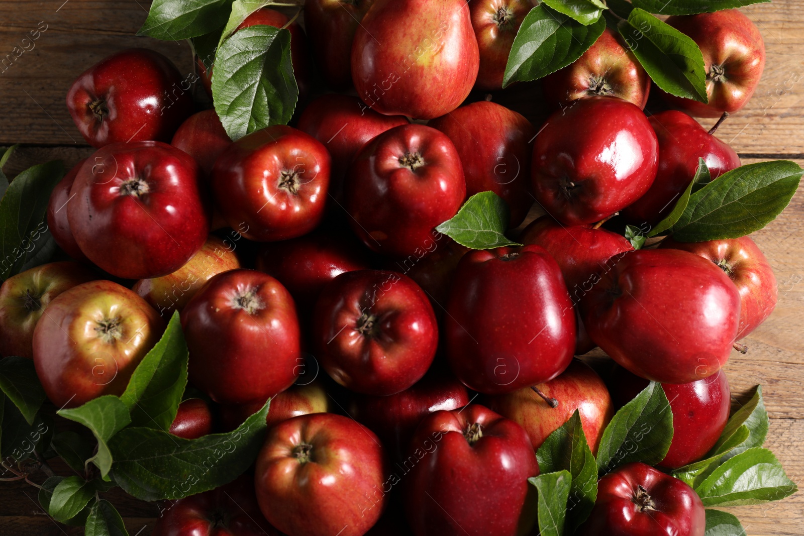 Photo of Fresh ripe red apples with leaves on wooden table, flat lay