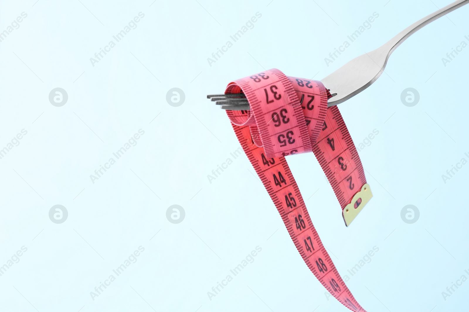 Photo of Fork with measuring tape on light blue background, space for text. Diet concept