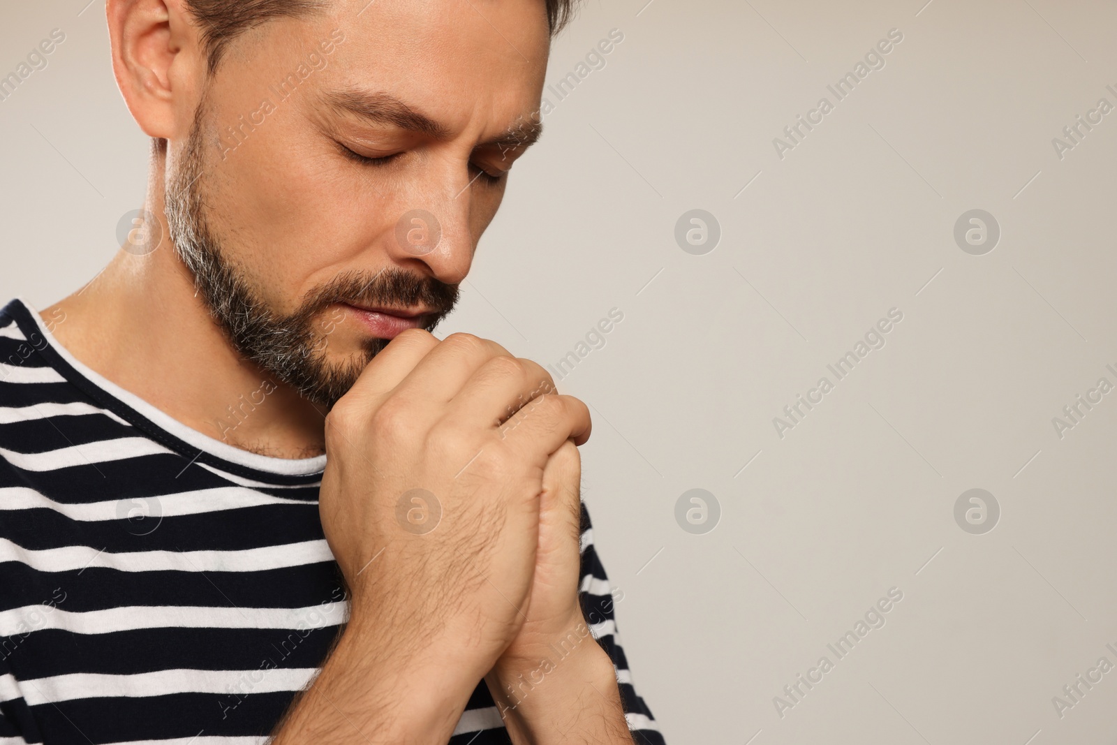 Photo of Man with clasped hands praying on light grey background, closeup. Space for text