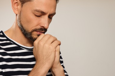 Man with clasped hands praying on light grey background, closeup. Space for text
