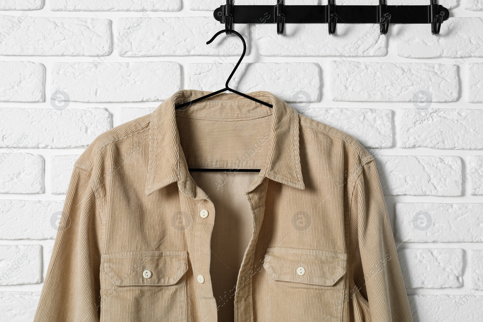 Photo of Hanger with beige shirt on white brick wall