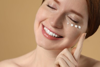 Photo of Smiling woman with freckles and cream on her face against beige background, closeup