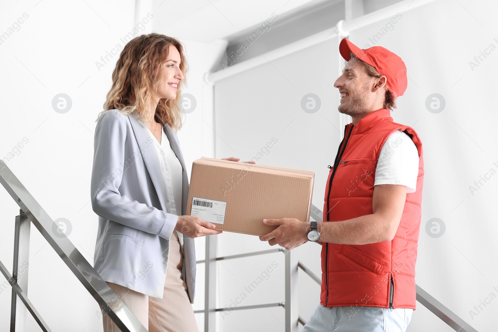 Photo of Young woman receiving parcel from courier indoors