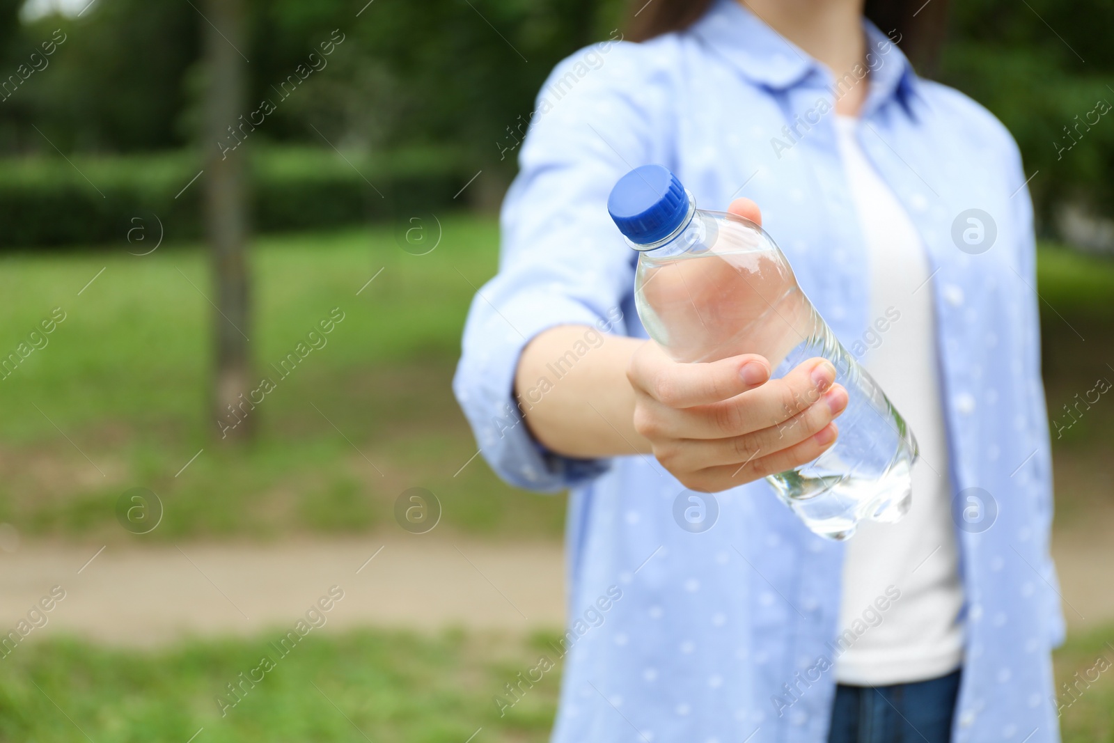 Photo of Woman holding bottle with water outdoors, closeup