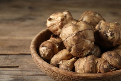 Photo of Bowl with fresh Jerusalem artichokes on wooden table, closeup