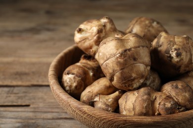 Bowl with fresh Jerusalem artichokes on wooden table, closeup