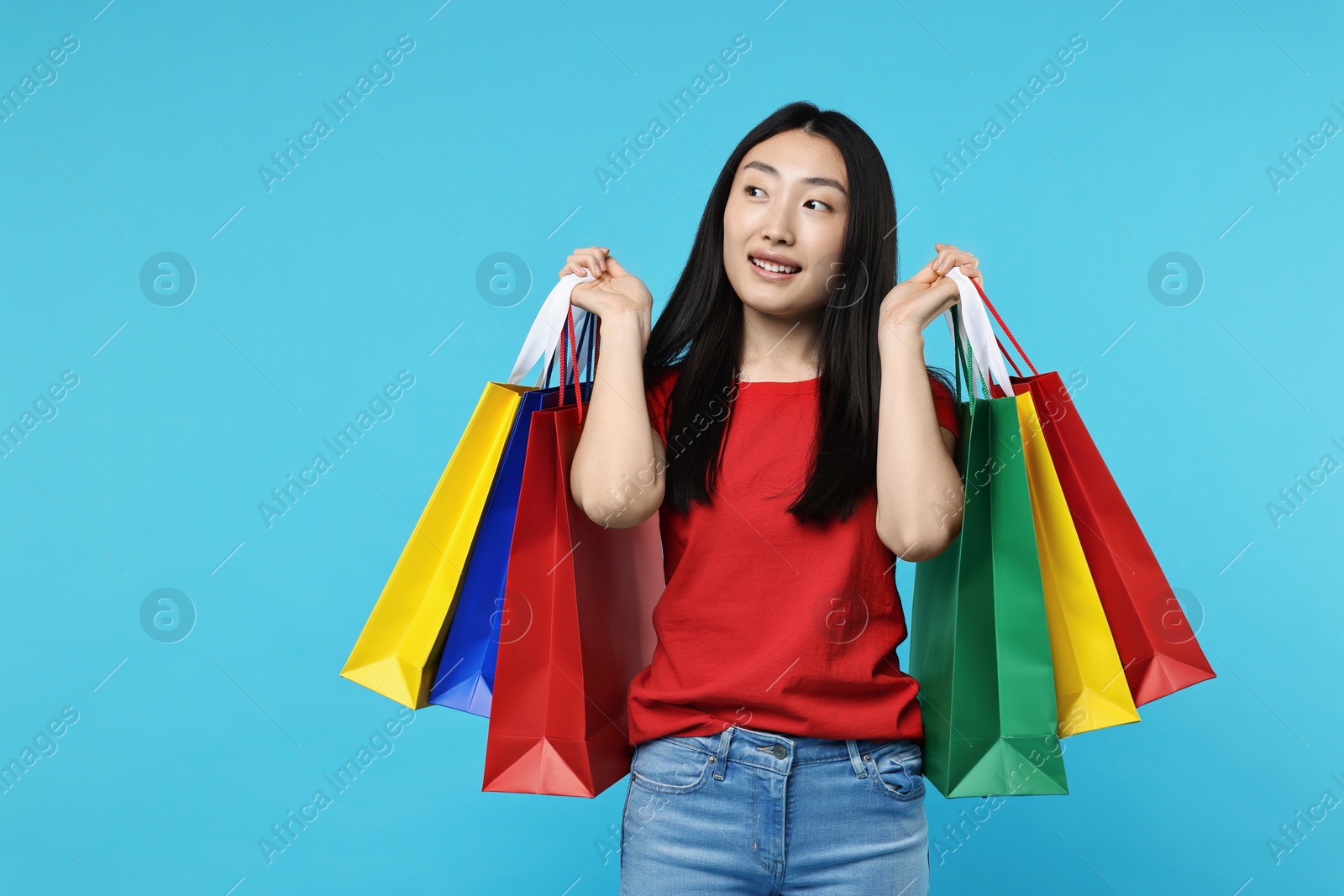 Photo of Happy woman with shopping bags on light blue background. Space for text