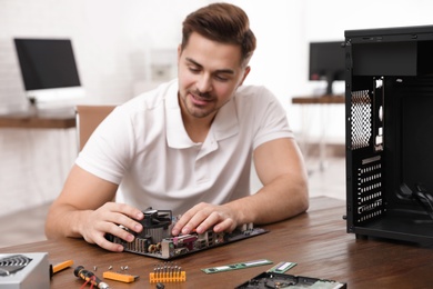 Photo of Male technician repairing motherboard at table indoors