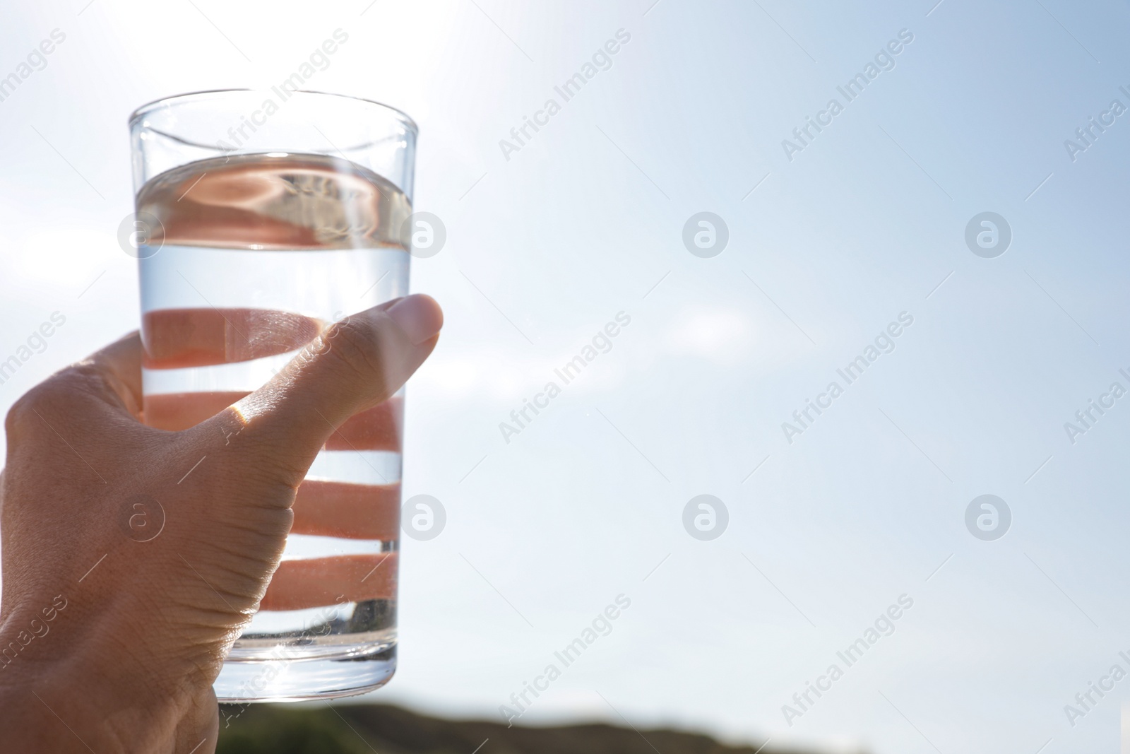 Photo of Woman holding glass of refreshing drink against blue sky on hot summer day, closeup. Space for text