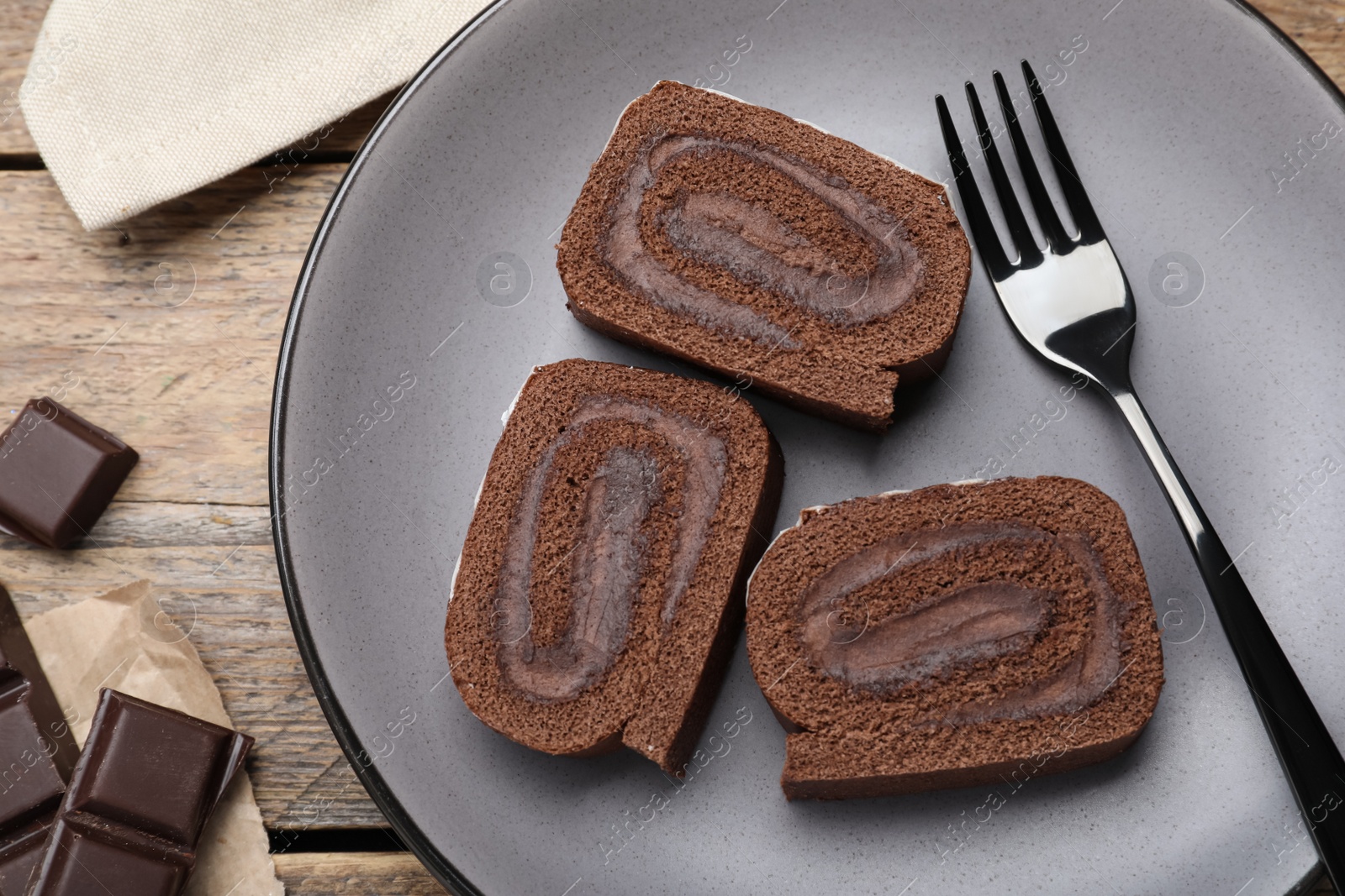 Photo of Tasty chocolate cake roll with cream on wooden table, flat lay