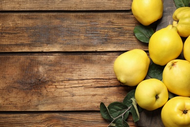 Fresh ripe organic quinces with leaves on wooden table, flat lay. Space for text