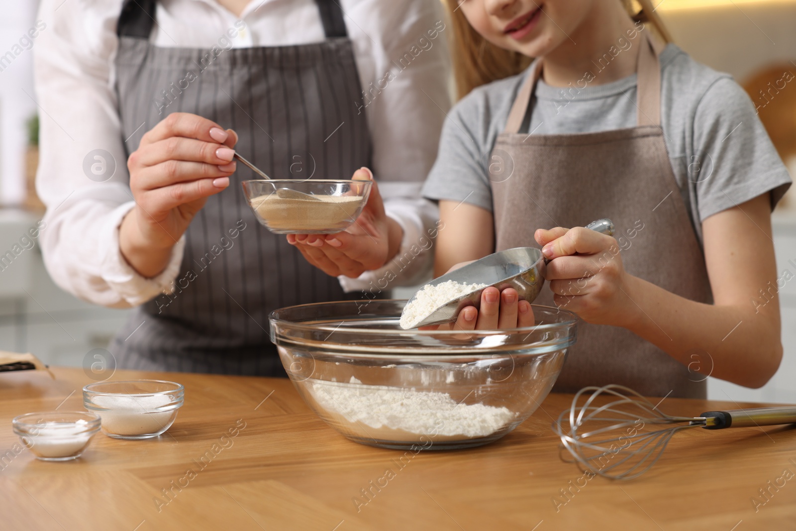 Photo of Making bread. Mother and her daughter putting flour and dry yeast into bowl at wooden table in kitchen, closeup