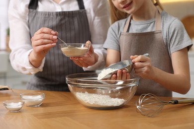 Making bread. Mother and her daughter putting flour and dry yeast into bowl at wooden table in kitchen, closeup