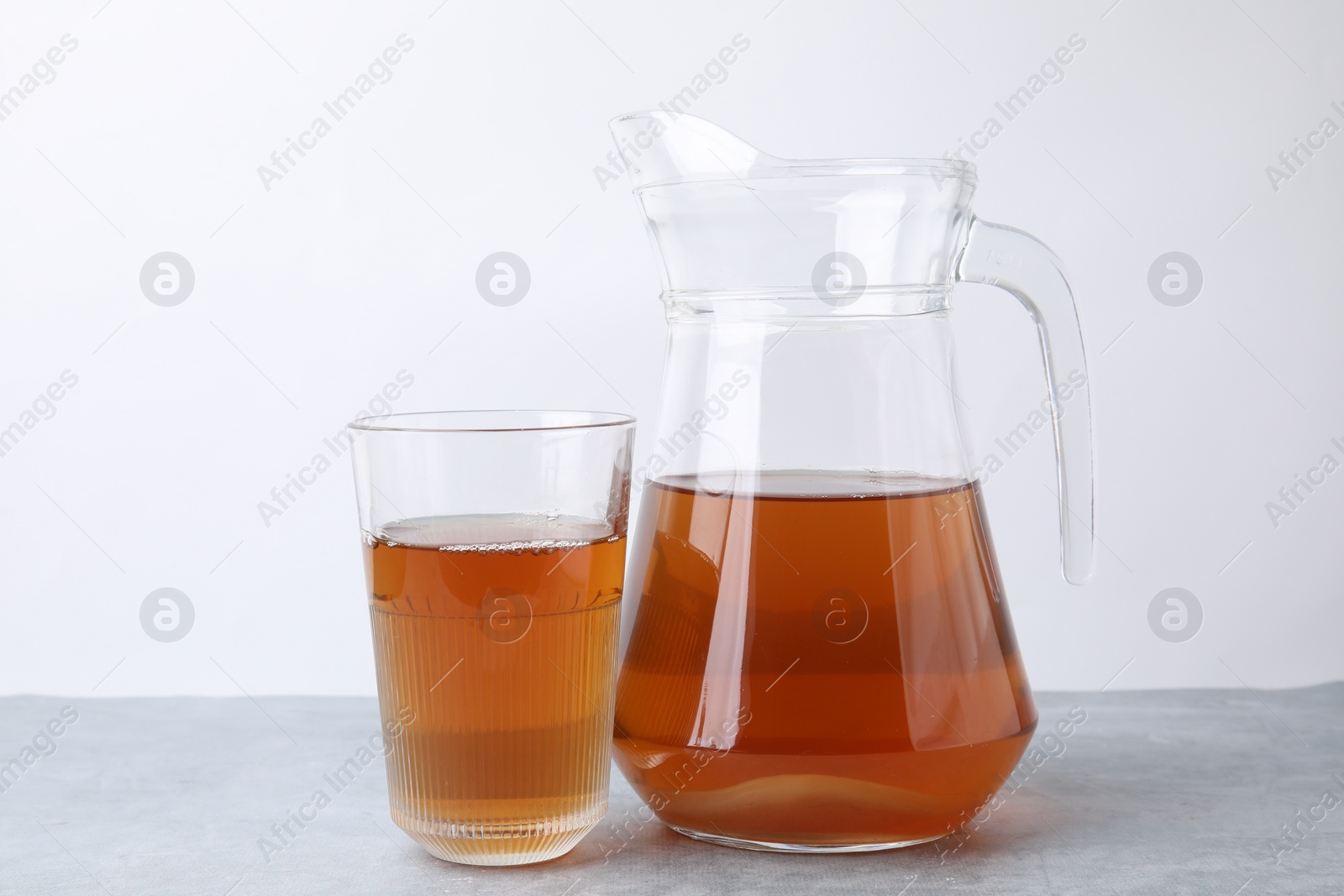 Photo of Homemade fermented kombucha in glass and jug on light grey table