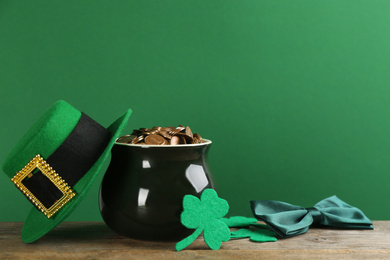 Composition with pot of gold coins and clover leaves on wooden table against green background. St. Patrick's Day celebration