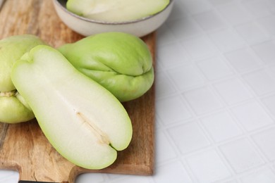 Photo of Cut and whole chayote on white tiled table, closeup. Space for text