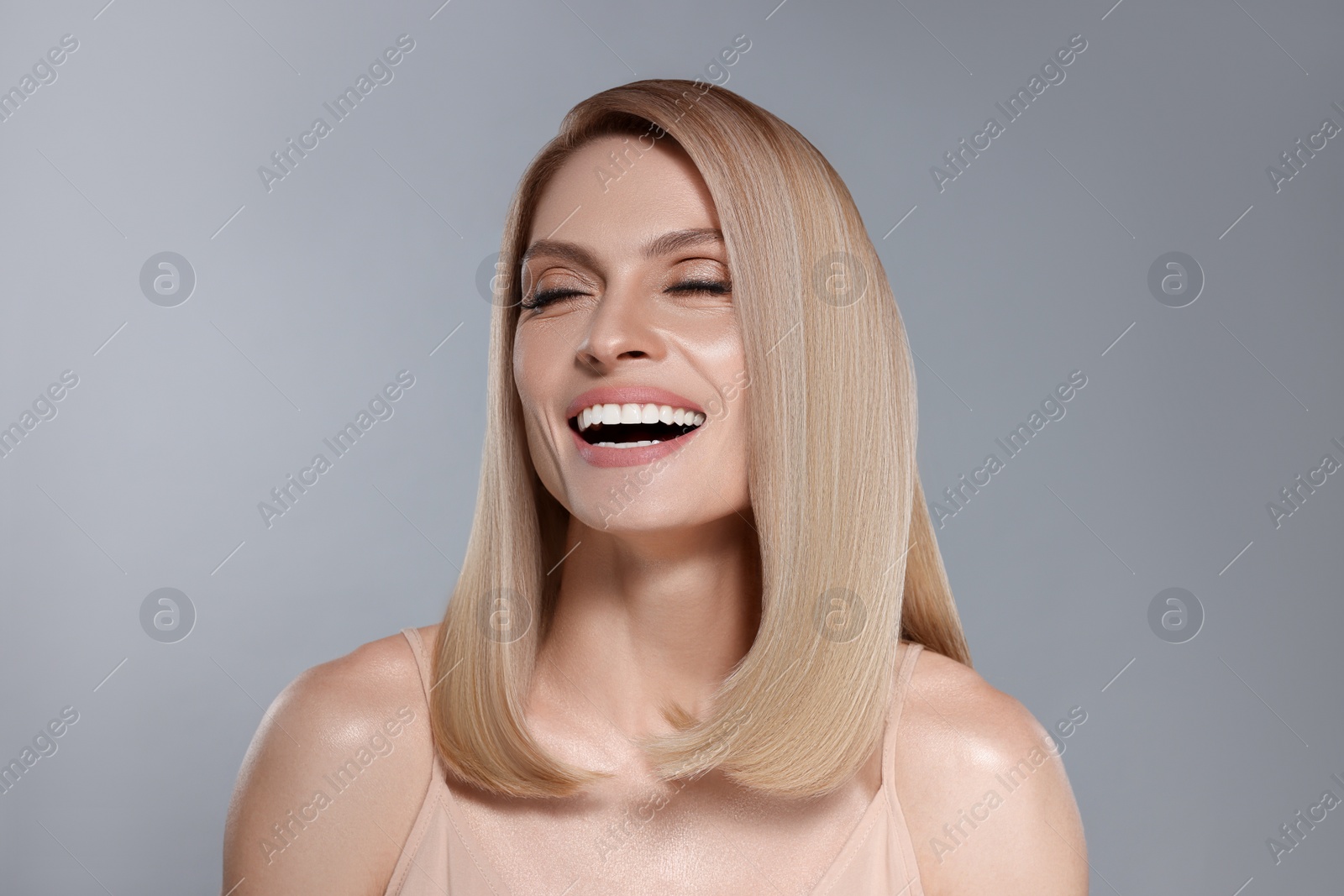 Image of Portrait of attractive woman with blonde hair smiling on grey background