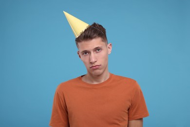 Sad young man in party hat on light blue background