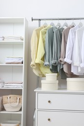 Wardrobe organization. Rack with different stylish clothes, shelving unit and chest of drawers near white wall