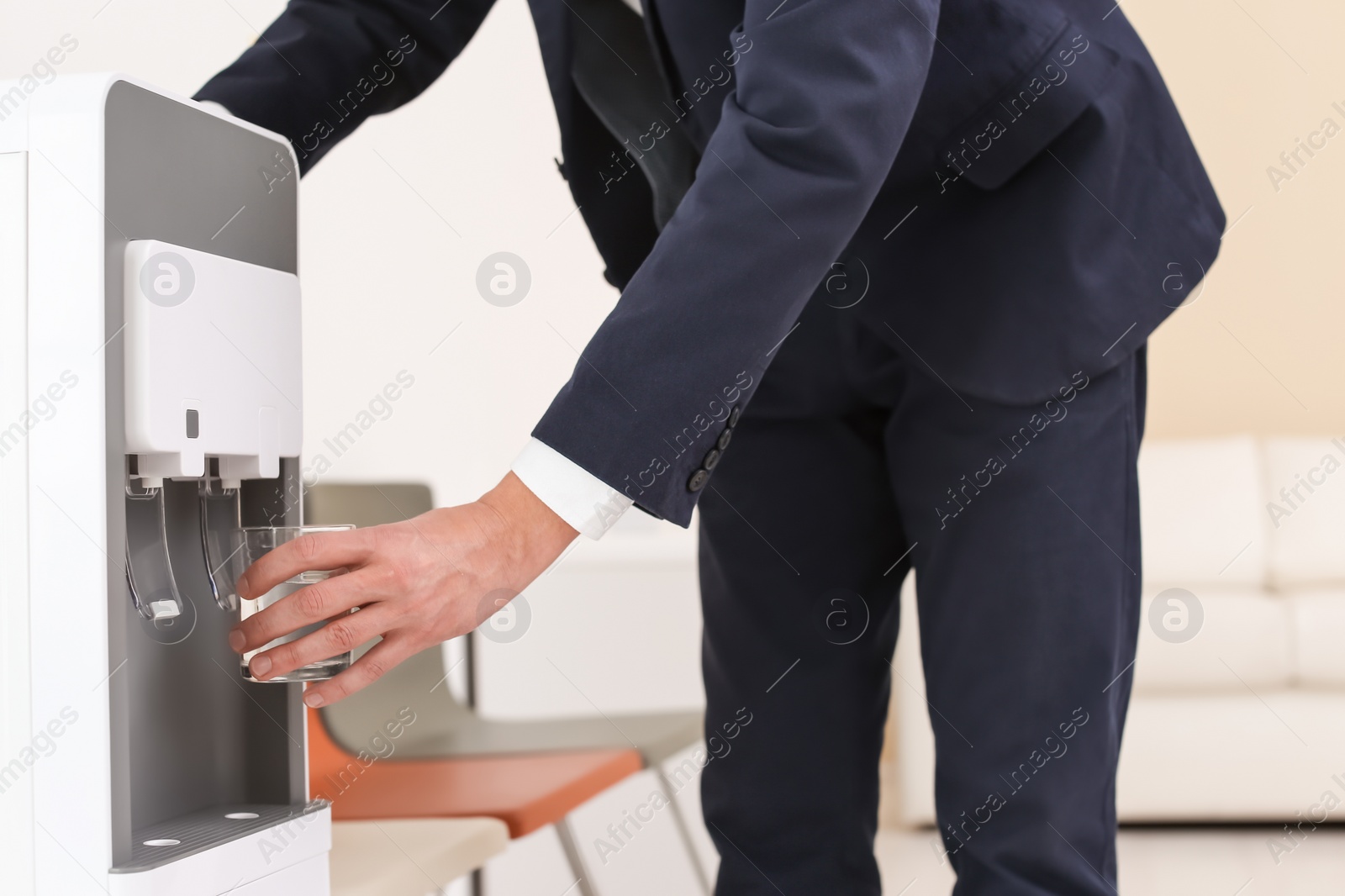 Photo of Man filling glass from water cooler indoors, closeup