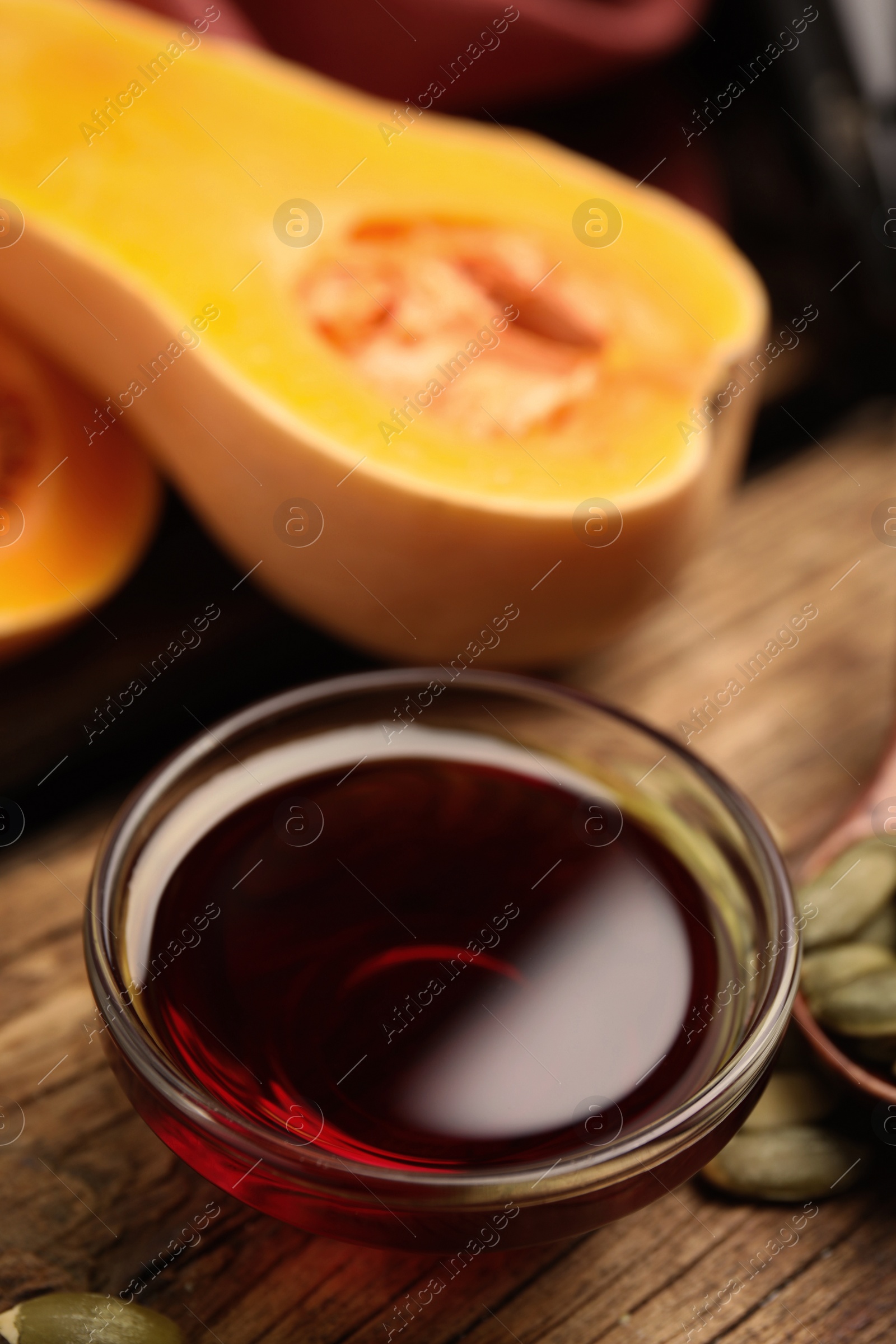 Photo of Glass bowl of pumpkin oil and seeds on wooden table, closeup