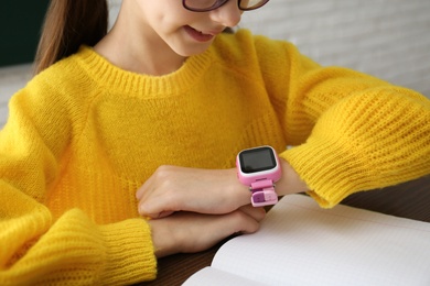 Photo of Girl with stylish smart watch at wooden table in school, closeup