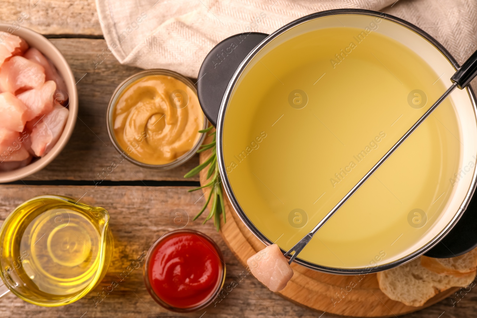 Photo of Fondue pot with oil, fork, raw meat pieces and other products on wooden table, flat lay