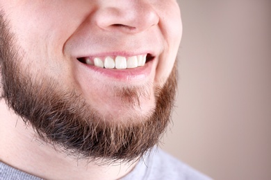 Young man with healthy teeth and beautiful smile on color background, closeup. Space for text